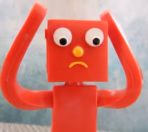 red robot toy looking confused with hands on his head in dismay