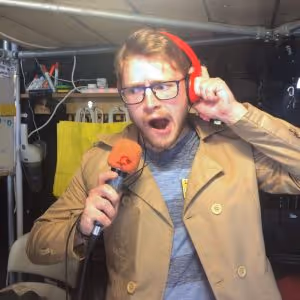 Man speaking in an orange microphone wearing orange headphones in Lockhouse Escape Games foyer