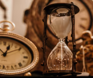 an hourglass with white sand in the timer next to a bronze coloured clock