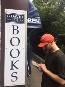 Man in red hat reading a book by a sign for G. David Bookseller's in Cambridge