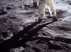 An astronaut suit from the waist down, casting a long humanoid shadow over the surface of the moon