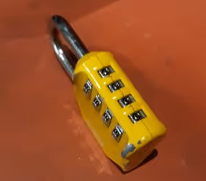 A yellow four digit padlock on a red background angled to show four zeros lined up in the correct code position
