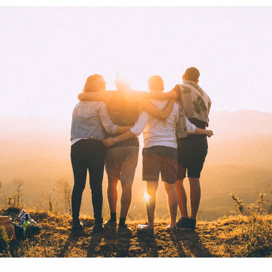 four people hugging on a mountain top at sunset