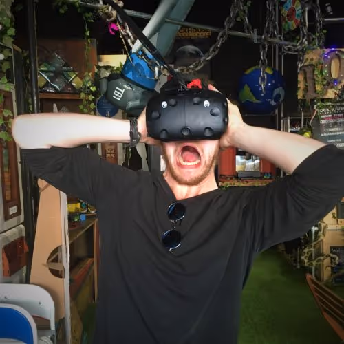 Man in LockHouse Escape Games Foyer, wearing a VIVE VR headset with googly eyes, looking alarmed
