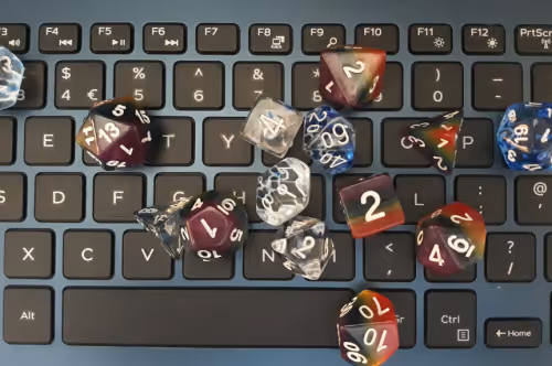 polyhedral dice for playing Dungeons and Dragons, some clear with blue streaks and some rainbow coloured, on top of a computer keyboard