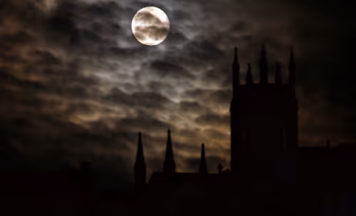 The moon shining through clouds over the misty silhouettes of buildings
