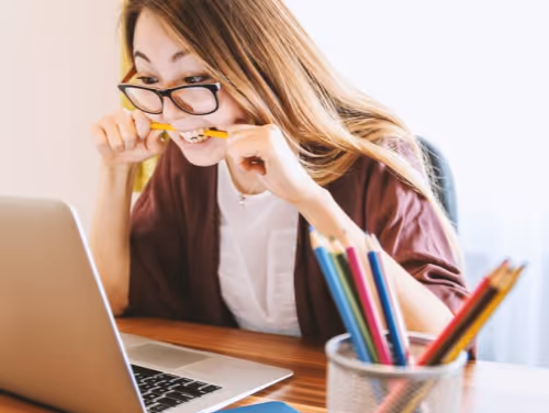 A student staring at a laptop screen with a stressed expression and chewing on a pencil