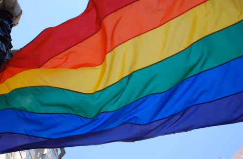 a rainbow pride flag flying in front of a blue sky