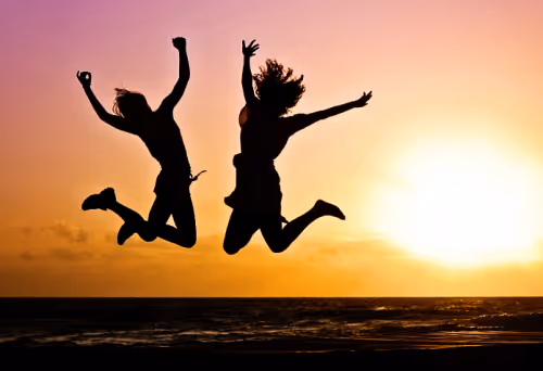 The silhouettes of two people jumping on a beach in front of a sunset