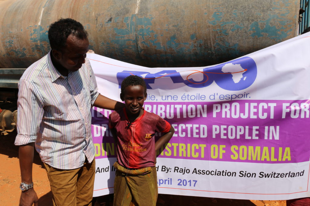 Un enfant pose fièrement devant un drapeau de l'association RAJO