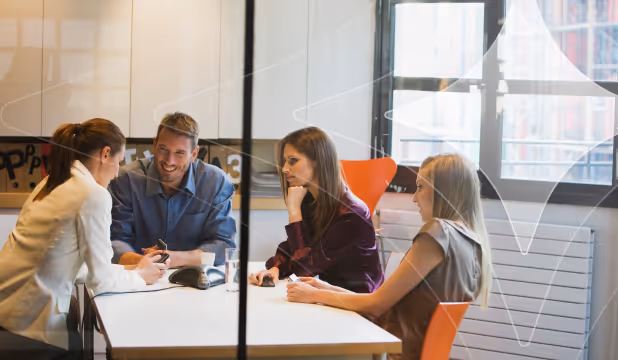 Four professionals engaged in a lively discussion around a white table in a modern office.