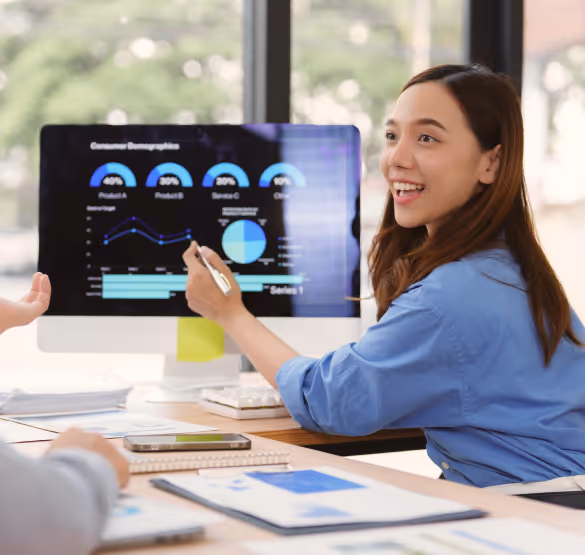 Woman in blue shirt pointing at a computer screen displaying data charts during a business meeting.