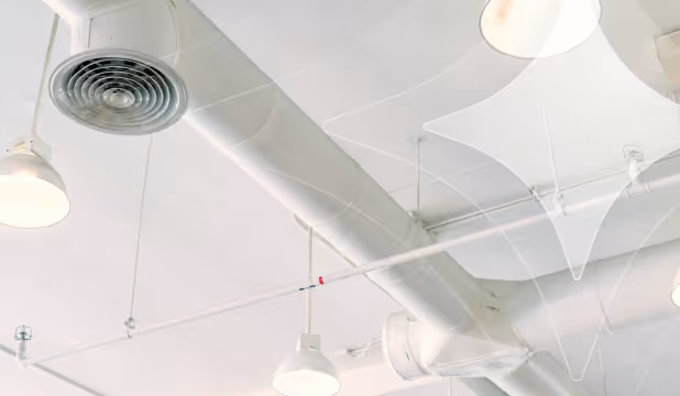 White ceiling with exposed ductwork, hanging cylindrical air vents, and suspended round lights.