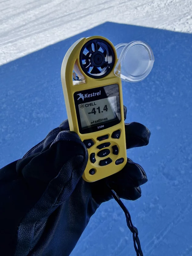 Hand wearing a black glove holding a yellow Kestrel 5500 weather meter showing a wind chill temperature of -41.4 degrees.