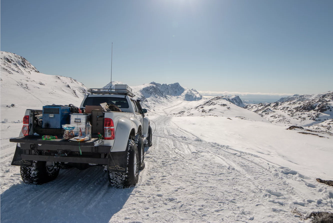 Pickup truck with equipment in the bed parked on a snowy mountain road under a clear blue sky.