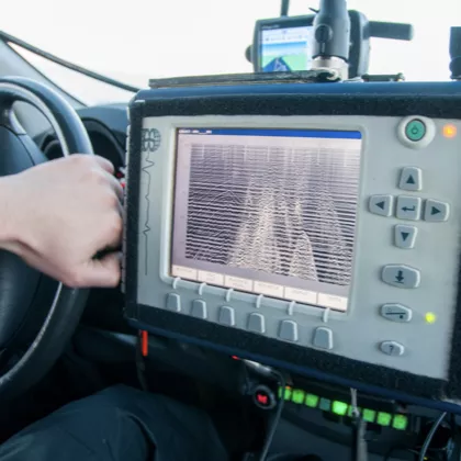 Close-up of a hand on a steering wheel next to a digital sonar or radar display screen inside a vehicle.