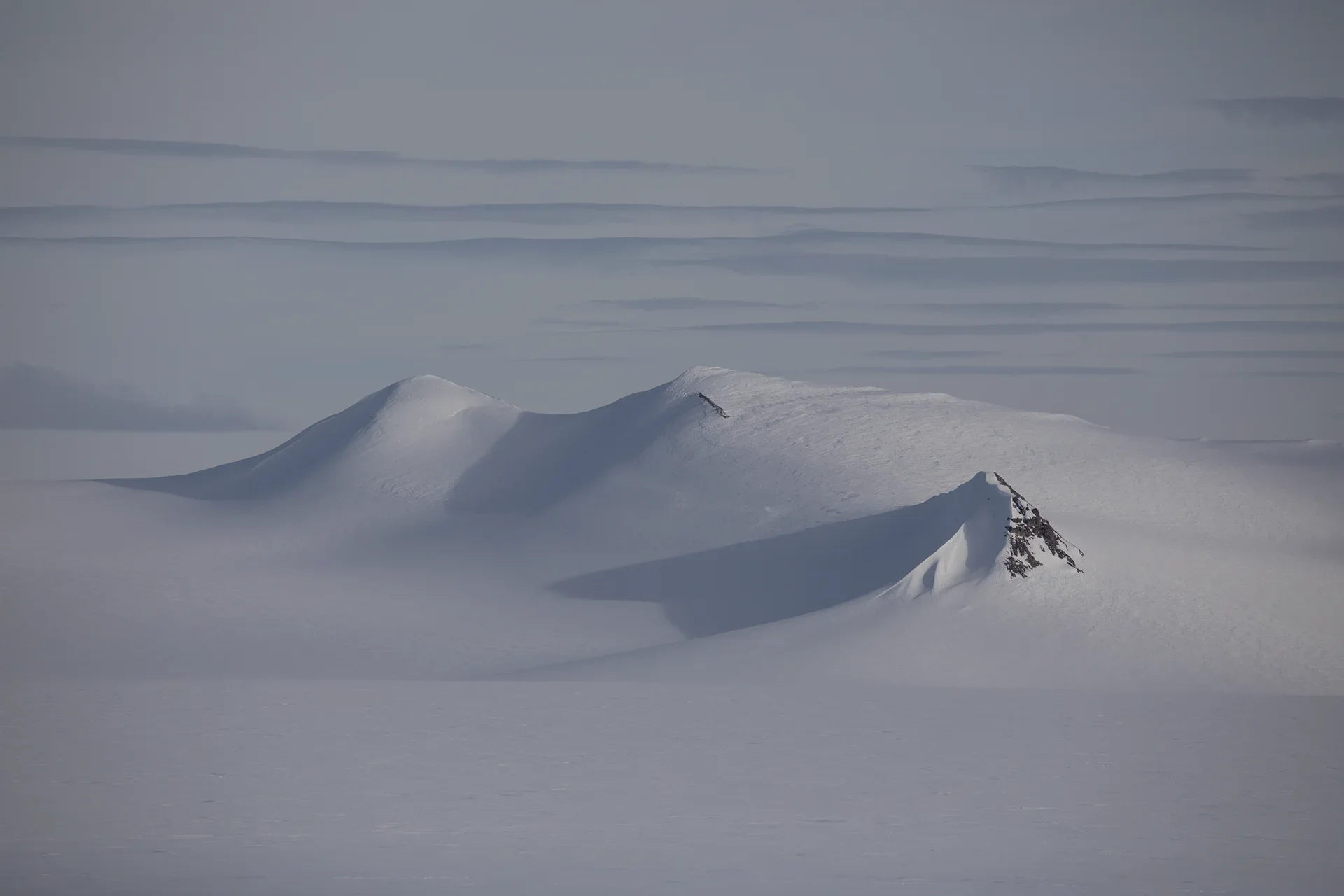 Snow-covered mountain peaks casting long shadows under a cloudy gray sky.