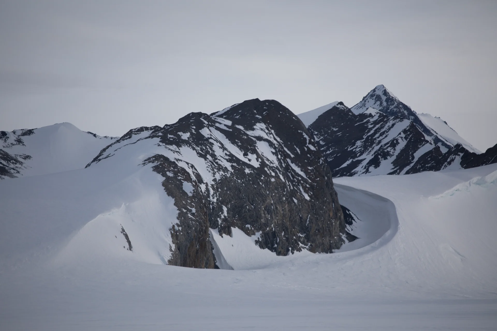 Snow-covered mountains with jagged peaks under a gray sky.