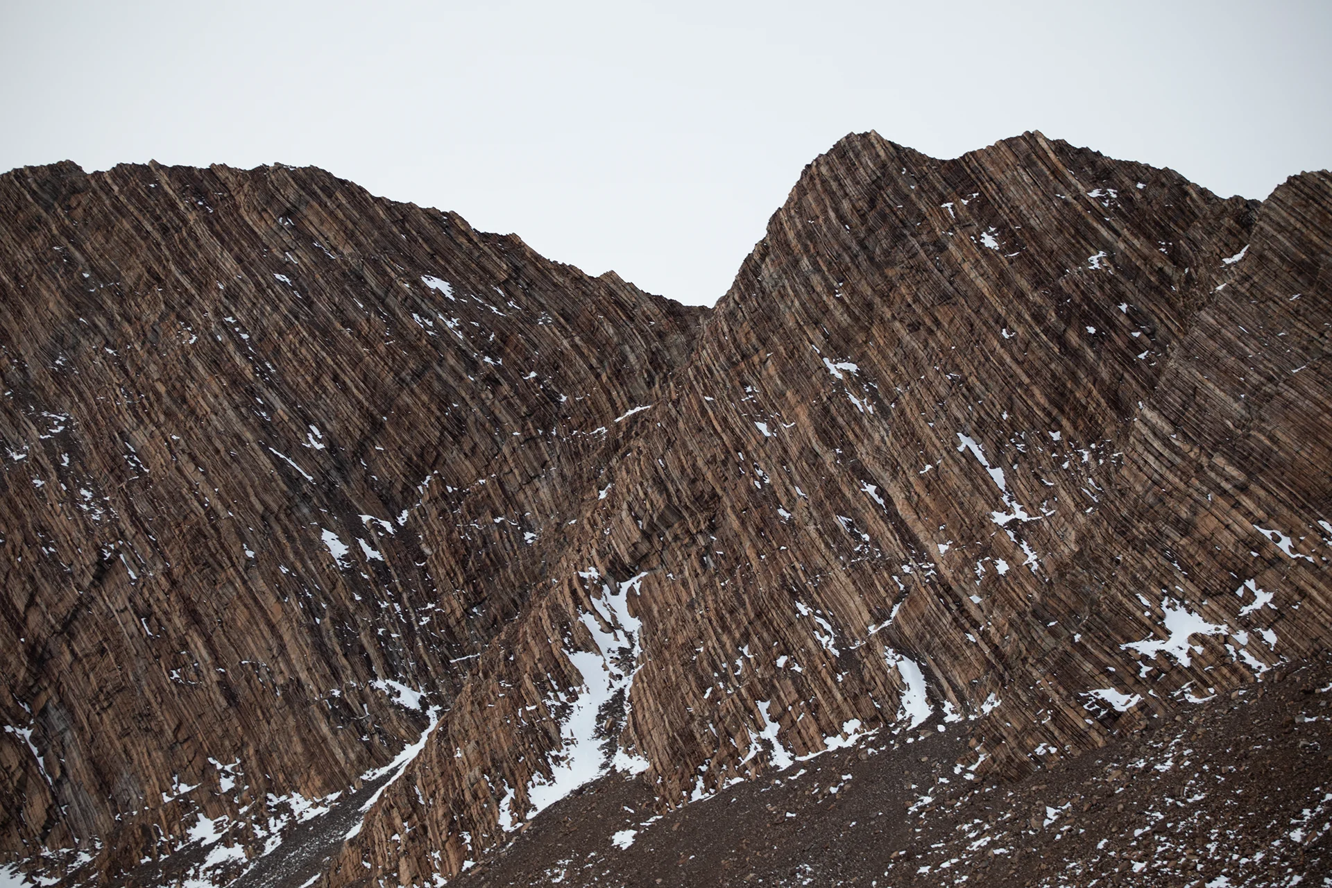 Close-up of steep rocky mountain ridges with snow patches under a pale sky.