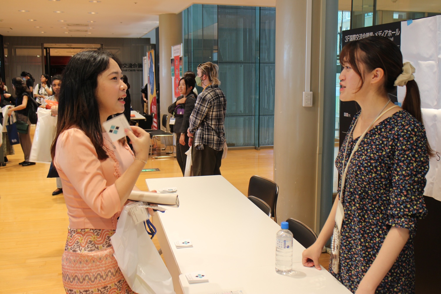 A woman with a joyful expression, eyes closed, and messy bun stands in a forest. She's wearing a choker and necklace. Light rain adds to the fresh, cheerful mood.