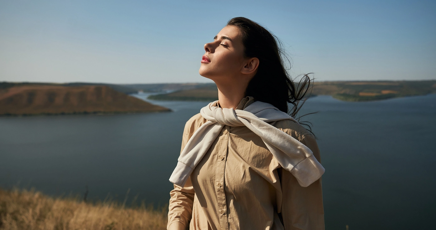a woman with her eyes closed standing in front of a body of water