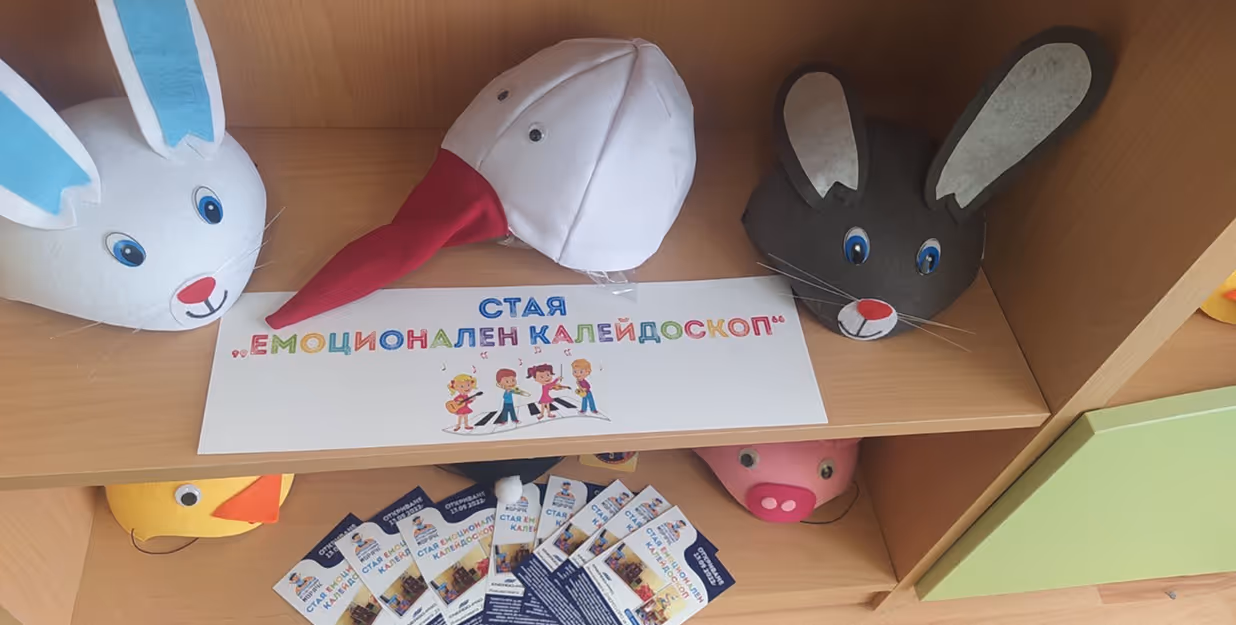 Emotion-focused educational display with animal hats and Bulgarian sign — Close-up of a wooden shelf showcasing handmade animal hats (rabbit, stork, mouse)