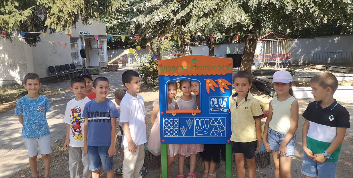 Kids playing with vegetable-themed outdoor learning board — Group of smiling children standing beside a colorful educational display titled “Fruits and Vegetables”