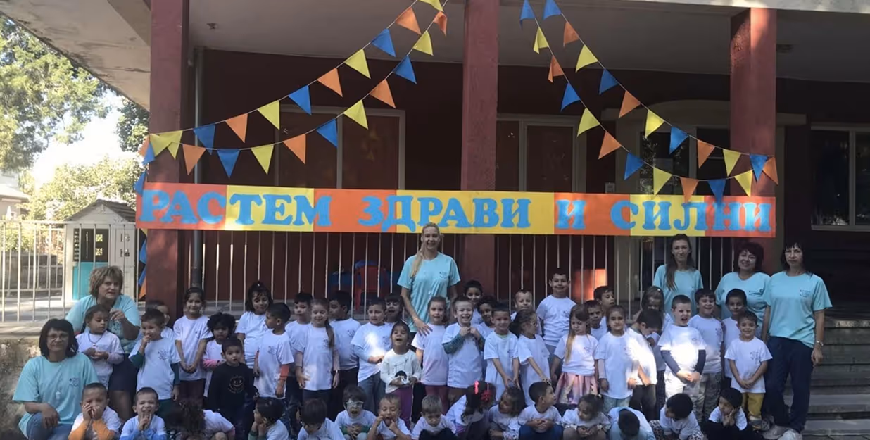 group of children and teachers at school health event — Large group of children in white T-shirts posing with teachers in mint-green uniforms in front of a banner