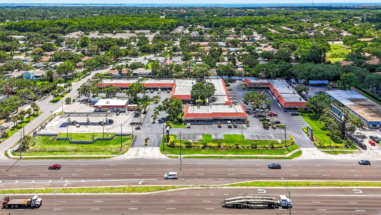 Aerial view of Palm Harbor Professional Center from across US Highway 19 North: low tile-roofed buildings set around a landscaped parking court, with neighbourhoods and tree canopy stretching to the water