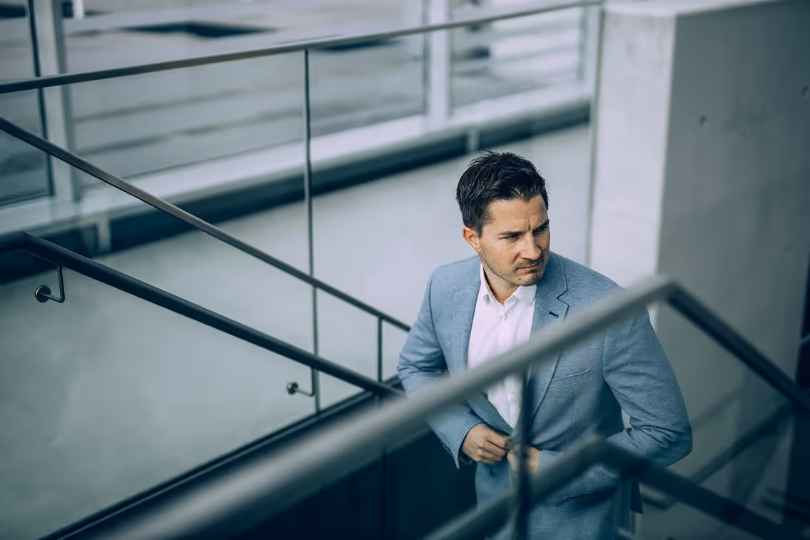 Mann im hellblauen Anzug, der eine Treppe in einem modernen Gebäude hinaufgeht und nach rechts schaut.