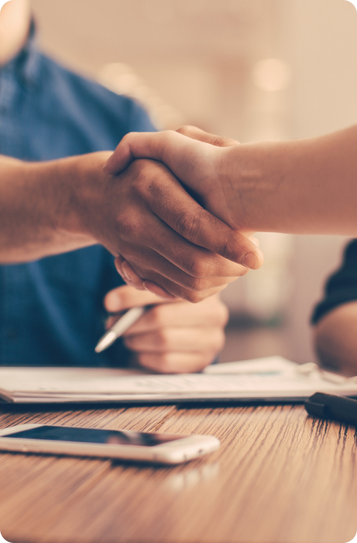 Two hands shaking over a desk with documents and phone