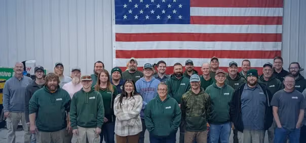 Team photo of workers in green shirts posing in front of American flag