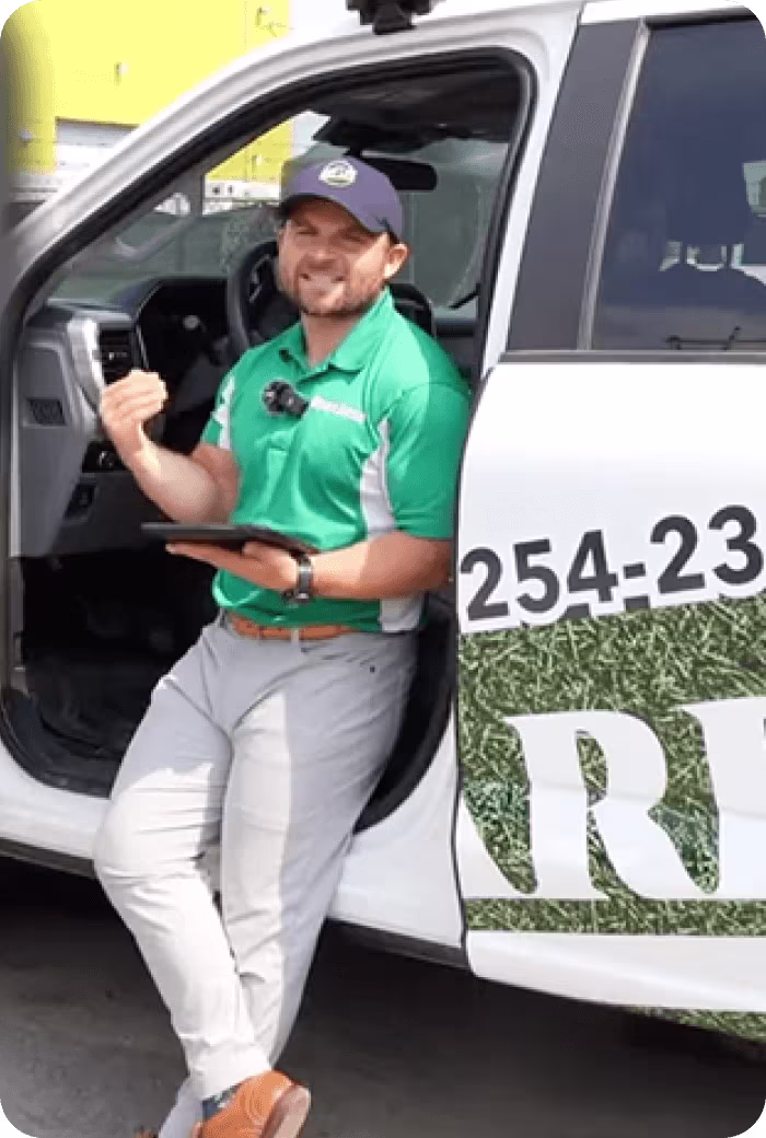 Smiling service worker in green shirt standing next to company vehicle