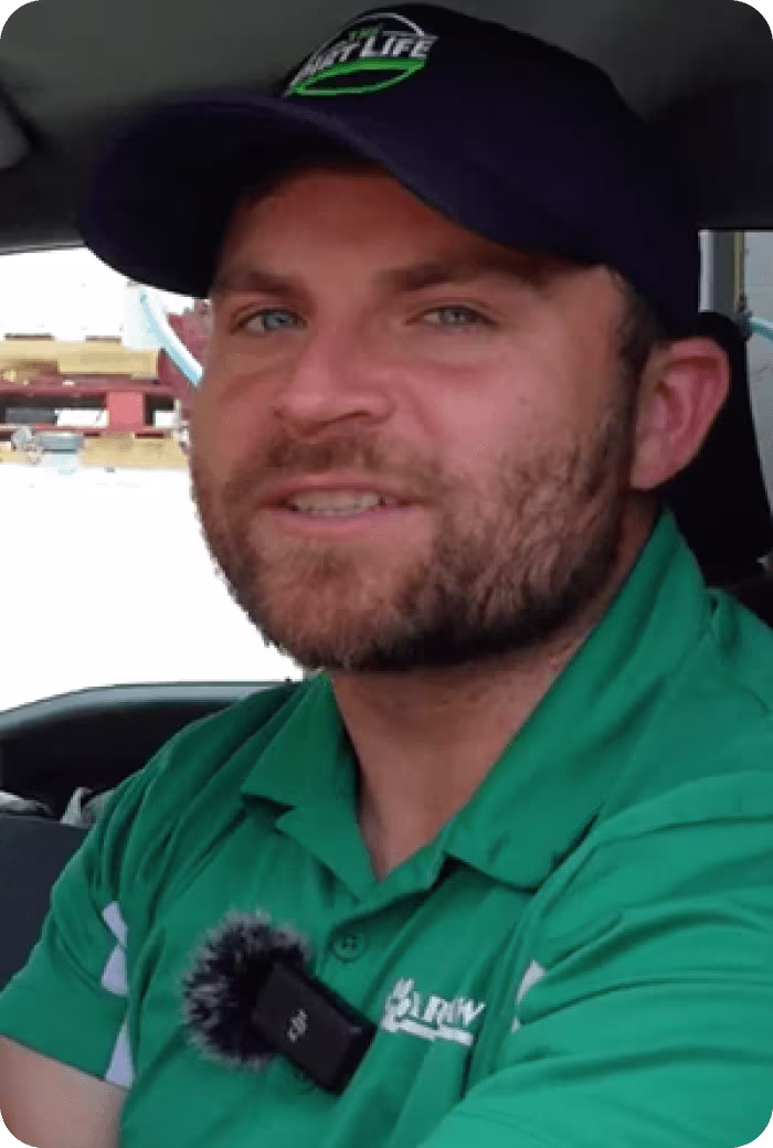 Smiling worker in green shirt and navy cap inside a vehicle