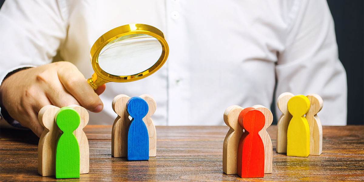 Colorful wooden figures under magnifying glass, representing diverse team analysis