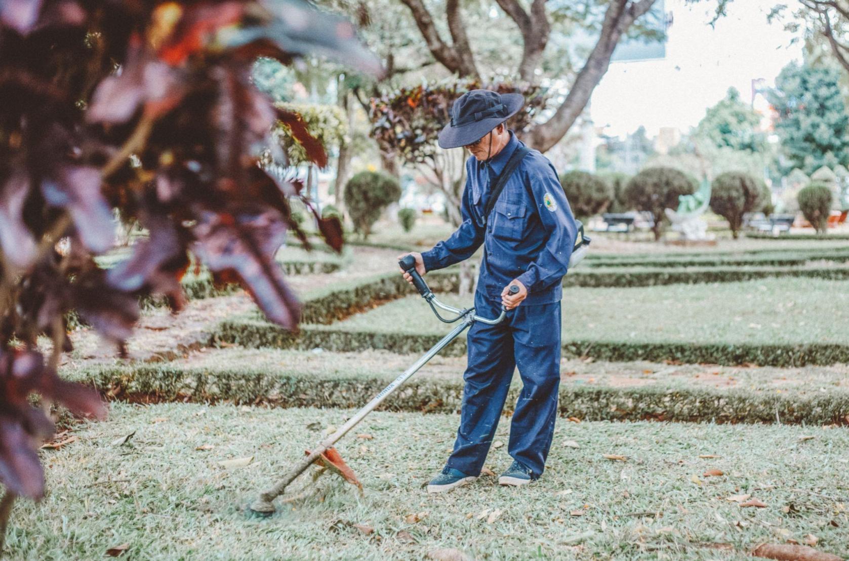 Gardener in blue uniform using string trimmer to maintain lawn