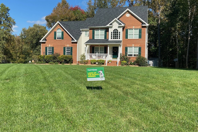 Brick two-story house with manicured lawn and lawn care sign