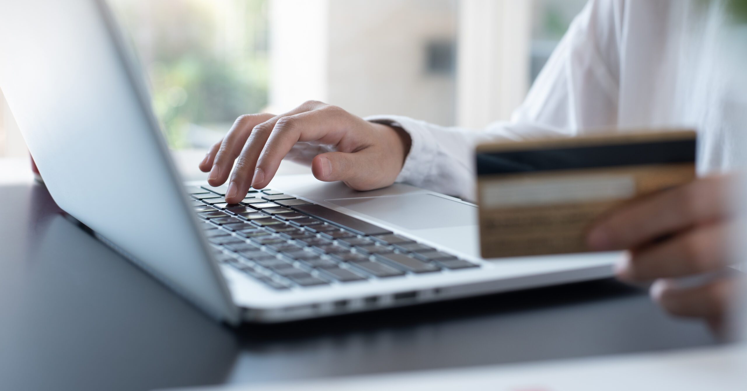 Hand typing on laptop keyboard while holding credit card for online purchase
