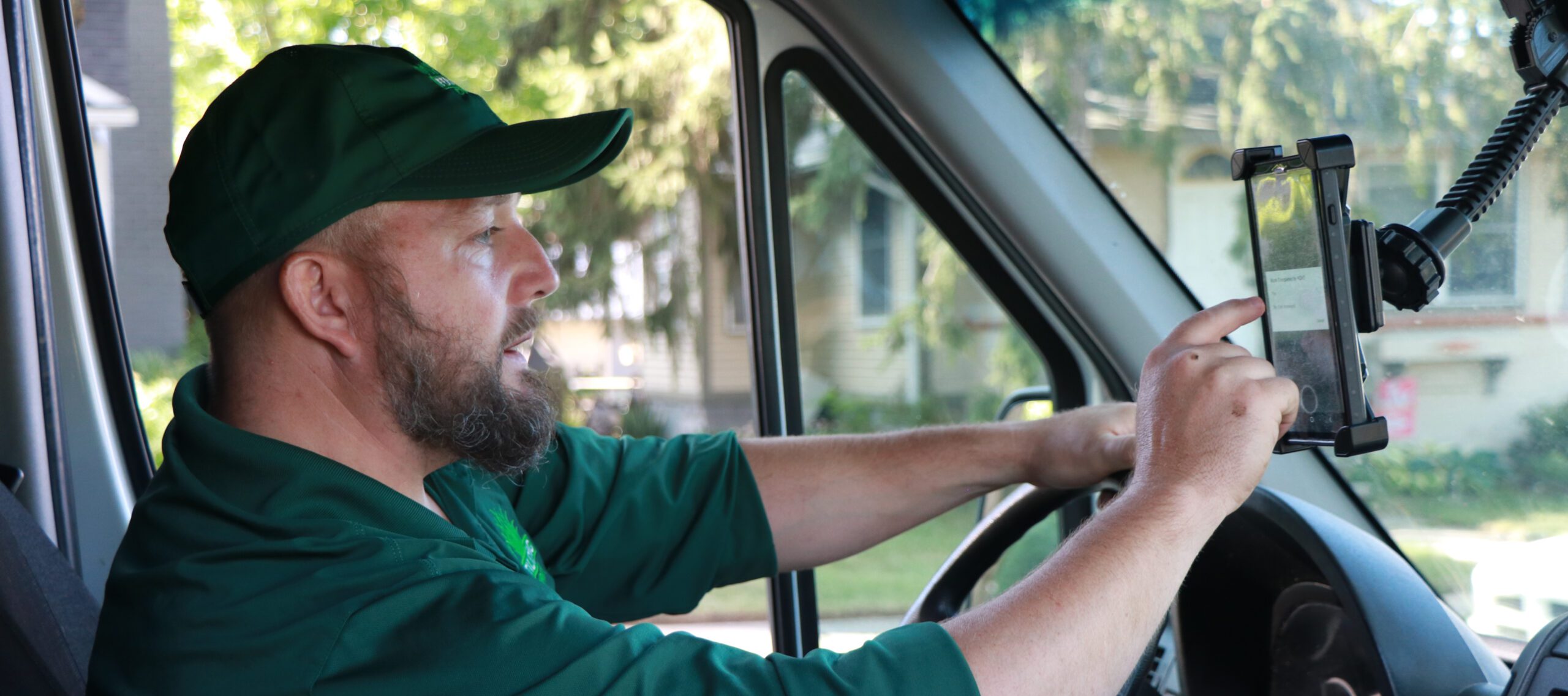Delivery driver in green shirt and cap adjusting GPS while driving