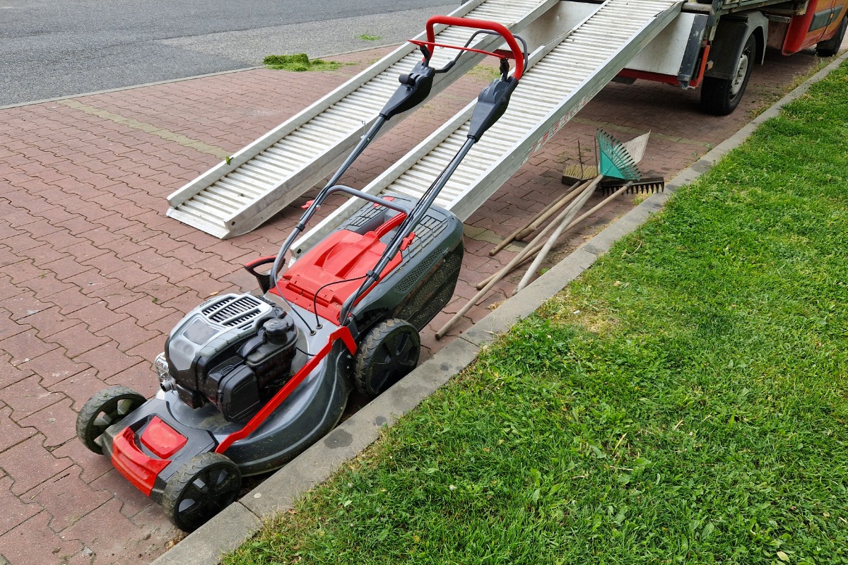 Red and gray lawn mower on brick path with garden tools nearby