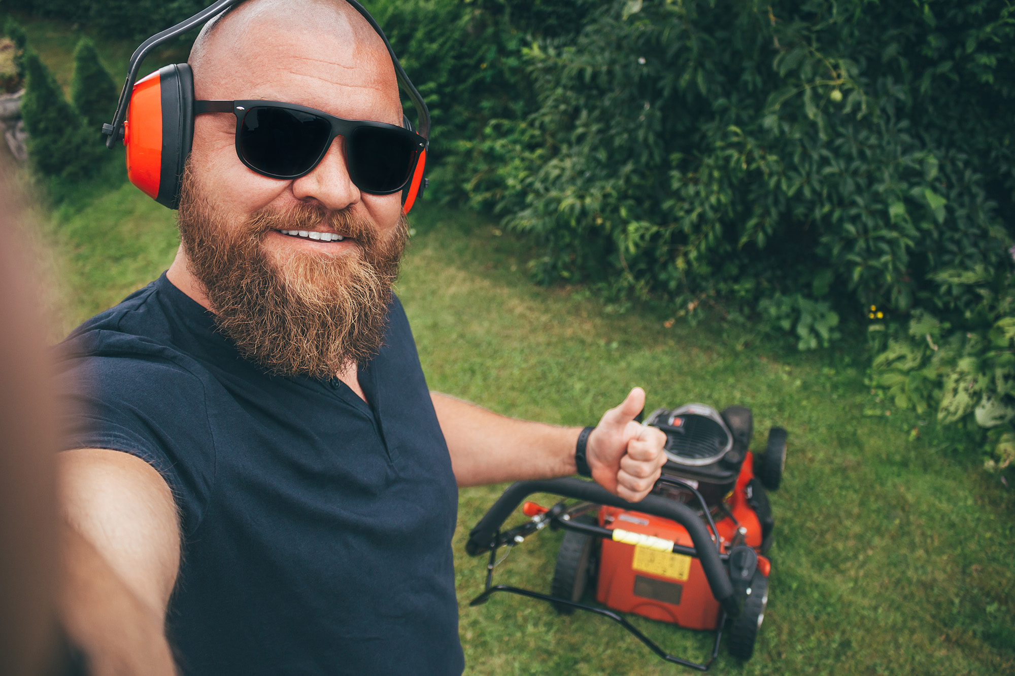 Bearded man with safety gear giving thumbs up near lawn mower