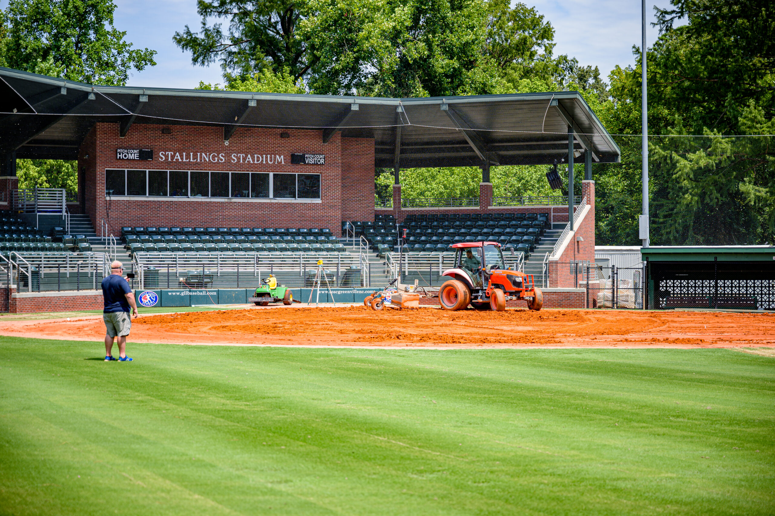 Orange tractor preparing baseball field at Stallings Stadium on sunny day