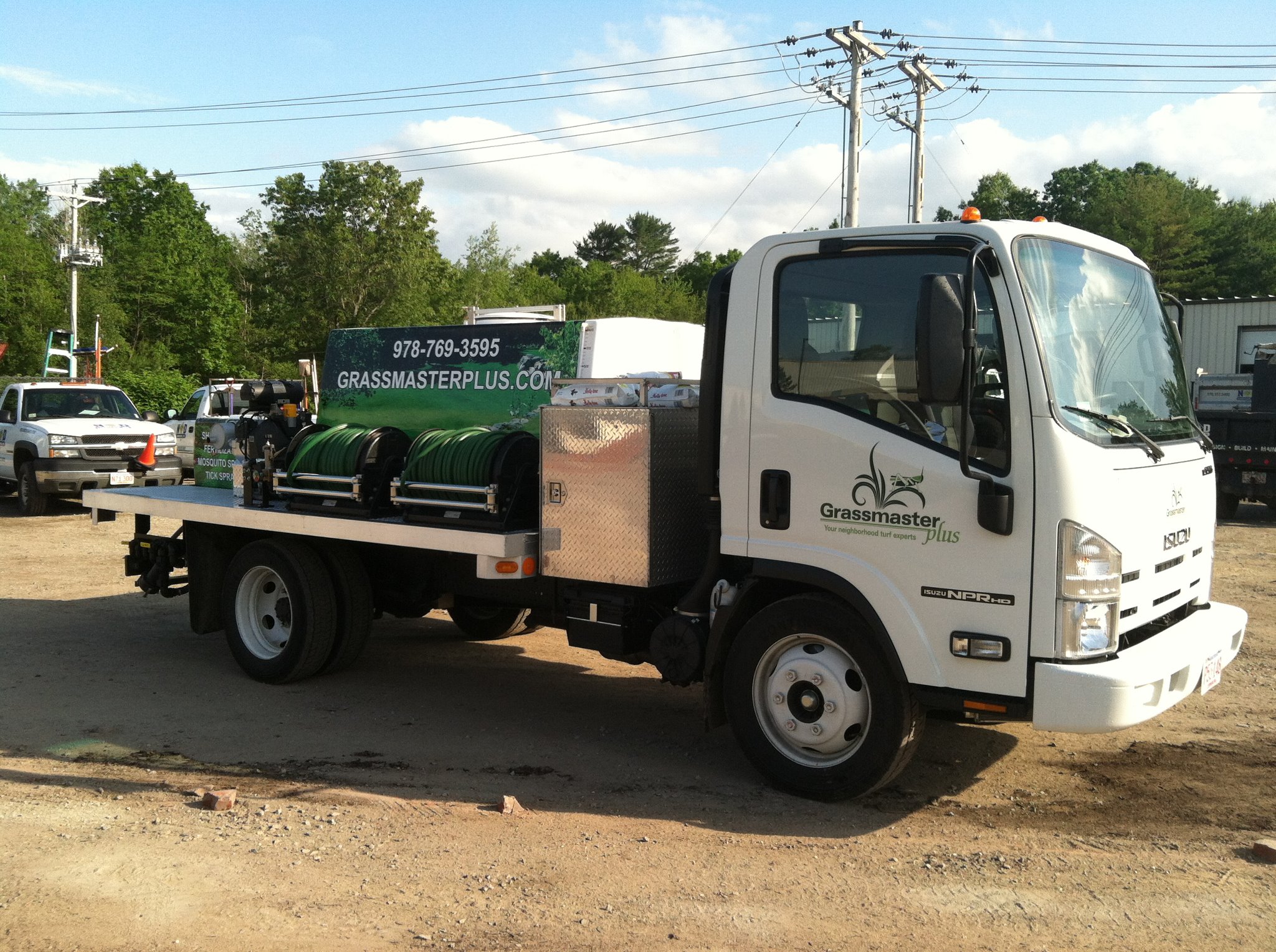 White Grassmaster Plus truck with green tanks parked on dirt yard
