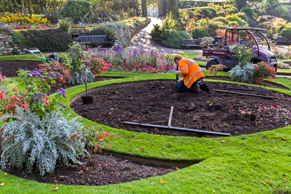 Gardener in orange vest working on circular flower bed in lush garden