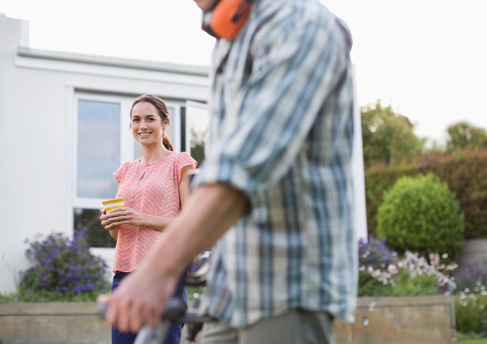 Person working in garden with hearing protection, another person smiling nearby