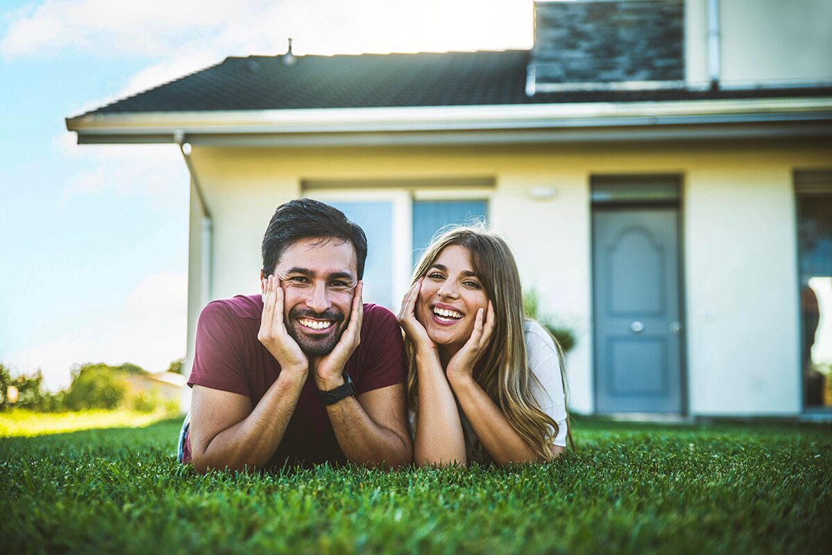 Happy couple lying on grass in front of their home, smiling