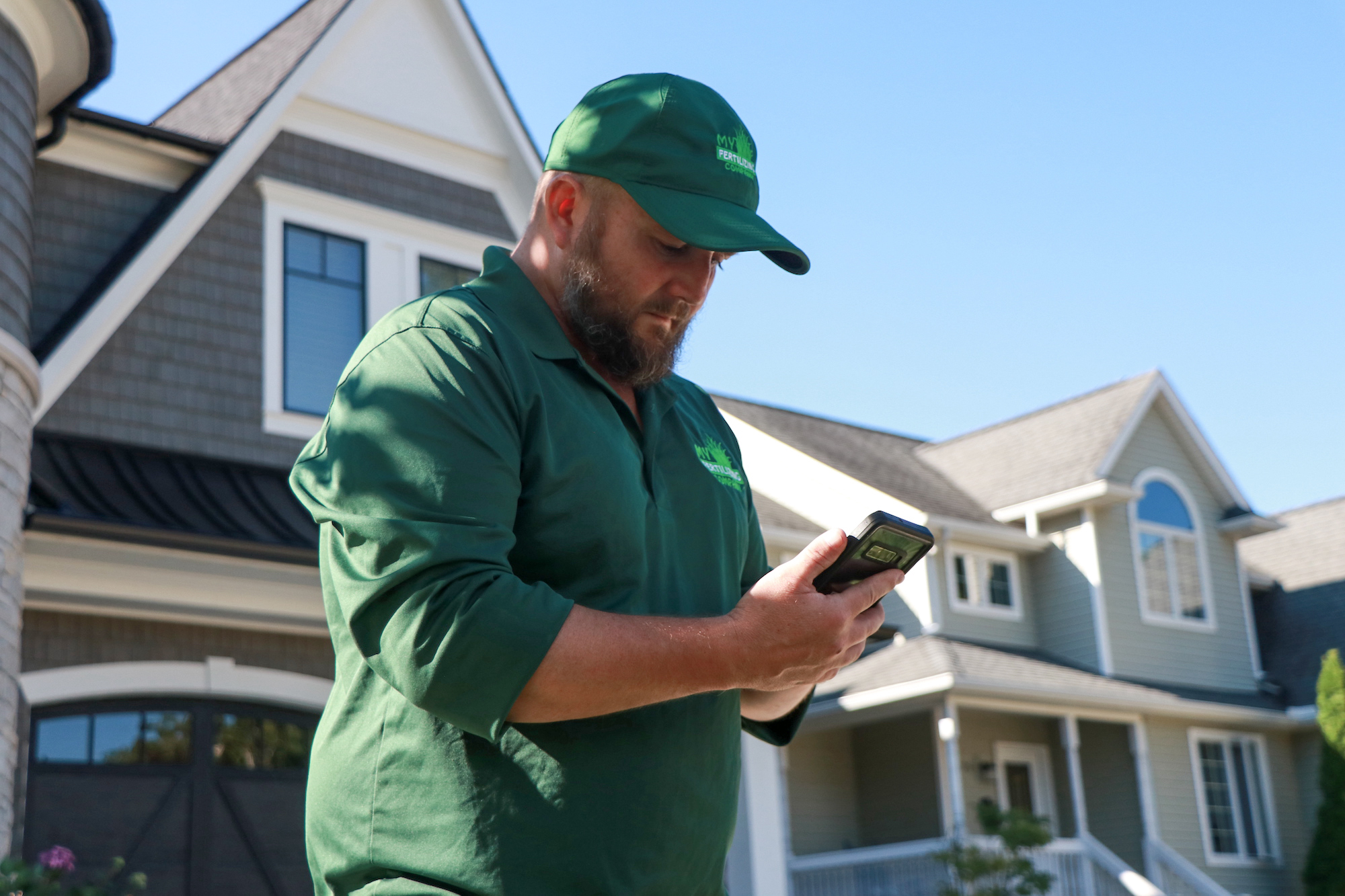 Pest control worker in green uniform checks phone near residential houses
