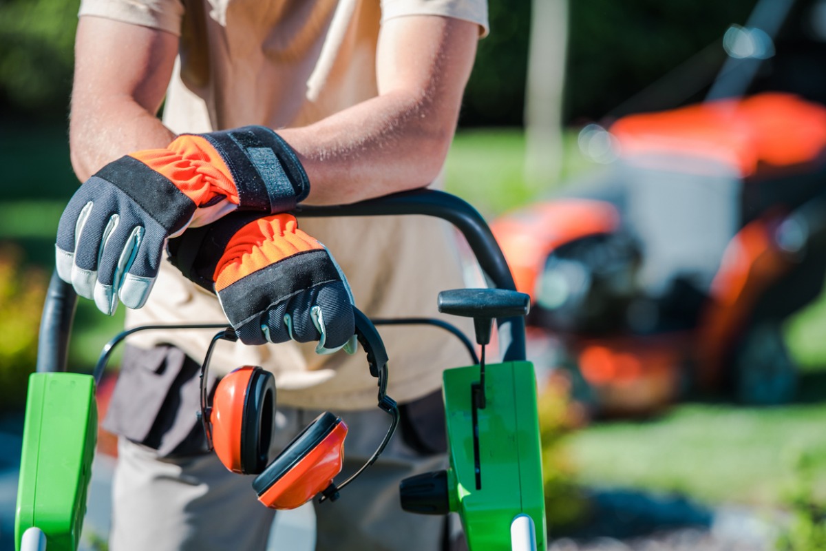 Gardener with safety gloves and ear protection operating lawn equipment