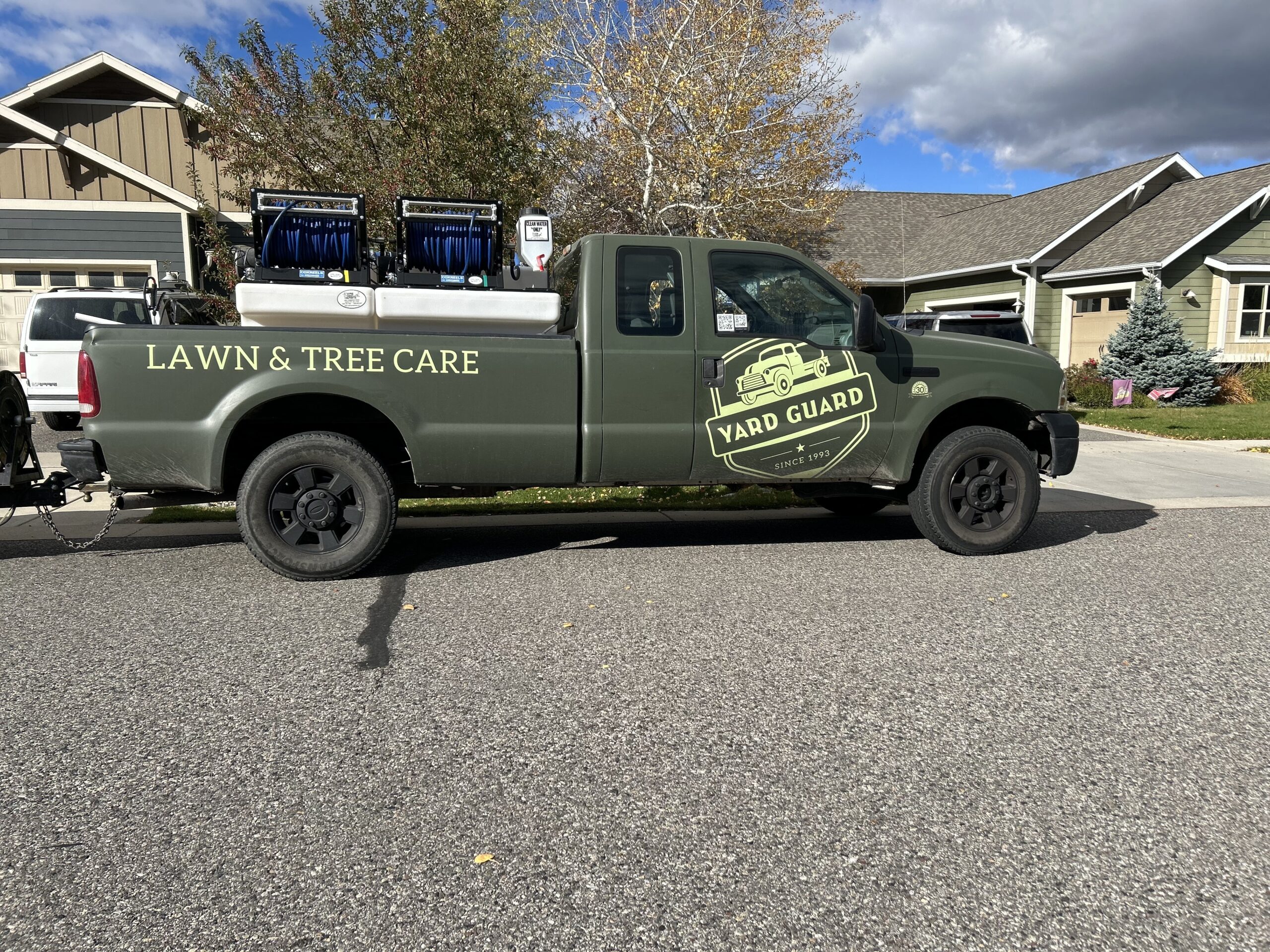 Green Yard Guard truck parked on street with lawn and tree care equipment