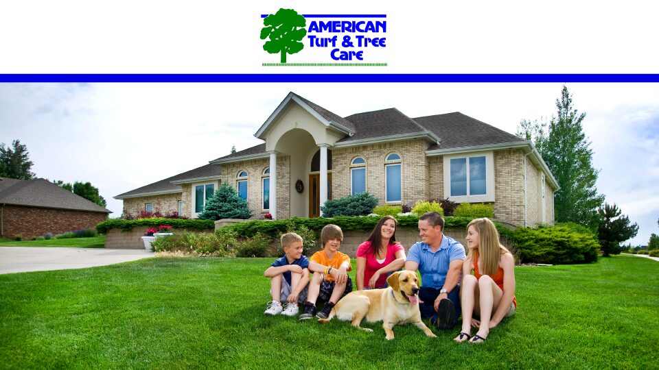 Family with dog sitting on green lawn in front of beautiful brick house